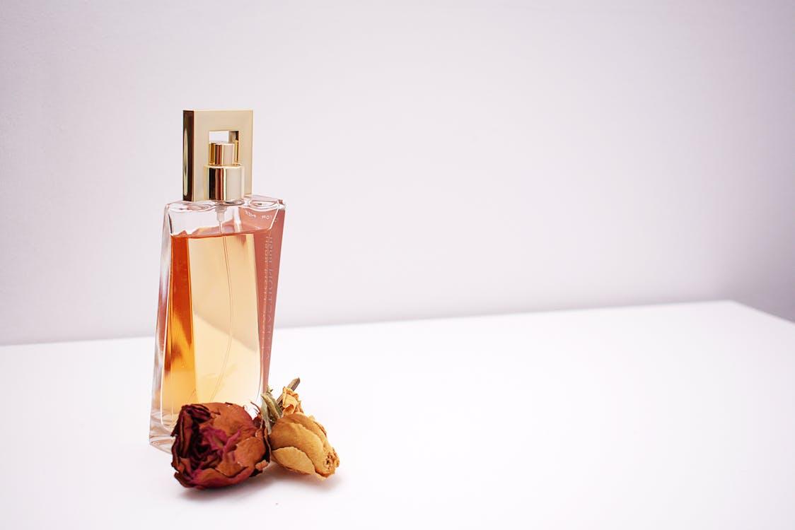 A perfume on a table with some flowers next to it. 