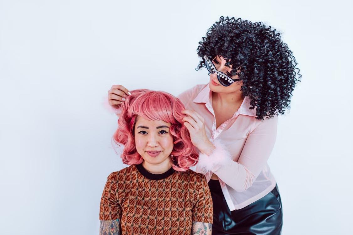 A person getting a pink color wig fitted on their head. 