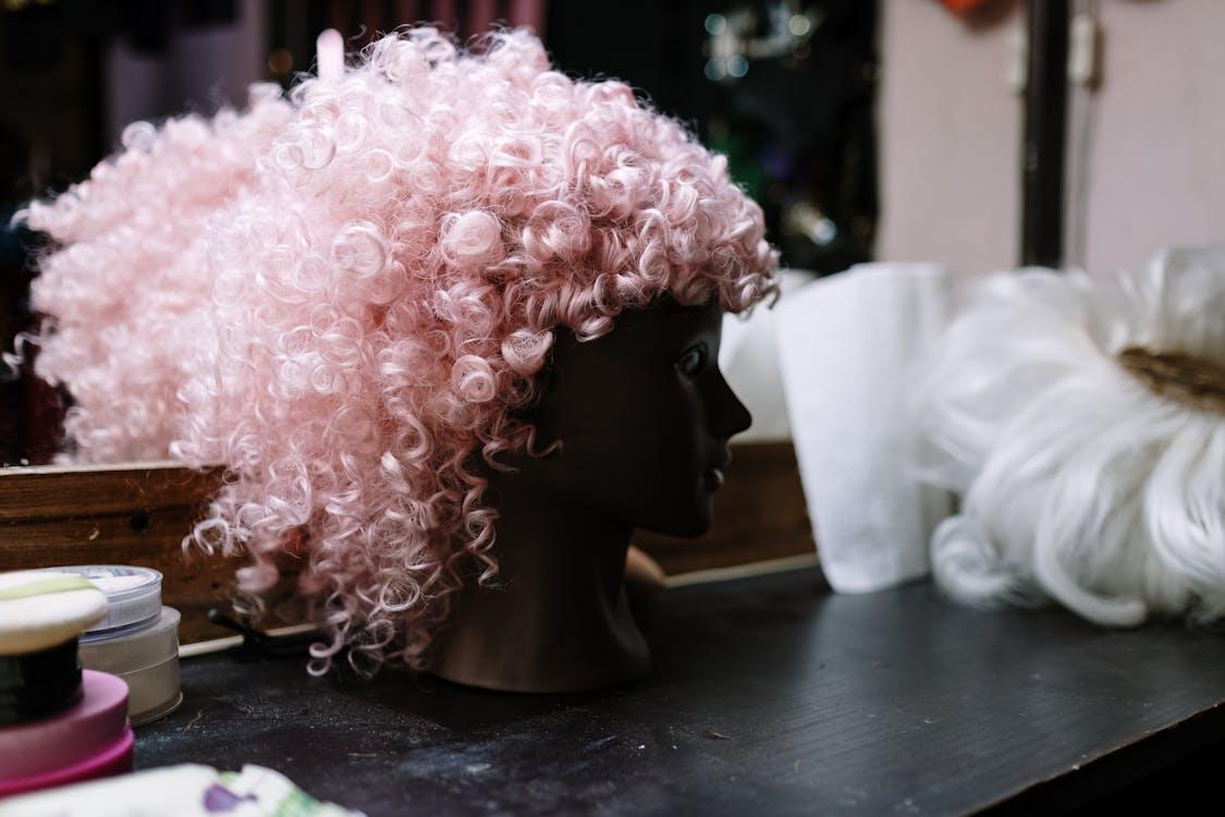 A pink colored wig placed on top of a dummy. 